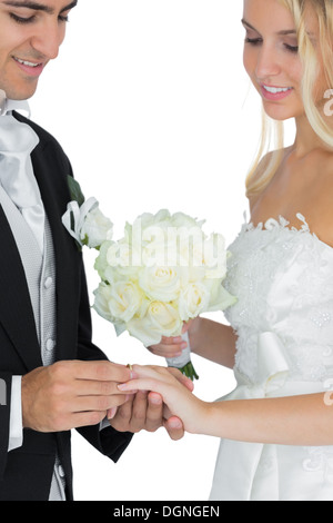 Smiling bridegroom putting the wedding ring on his wife's finger Stock Photo