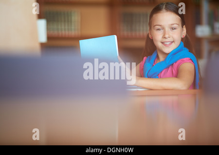 Portrait of a lovely girl looking at camera while reading in library Stock Photo