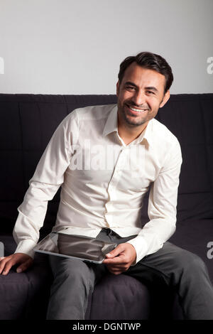 Smiling man sitting on a sofa with an iPad Stock Photo