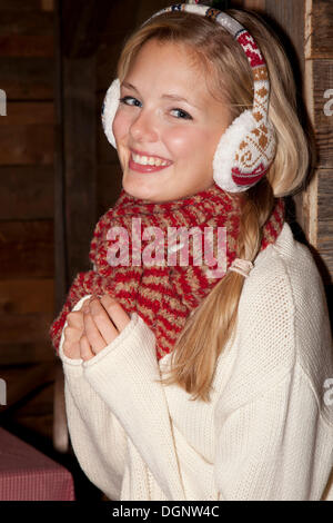 Smiling young woman wearing ear warmers and a scarf in a hiking hut Stock Photo