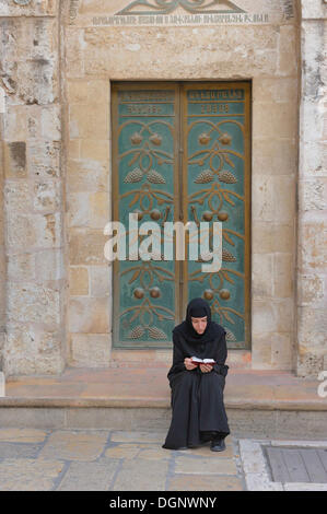 Russian Orthodox nun praying in front of the door of the Church of the Holy Sepulchre, Christian Quarter in the Old City of Stock Photo