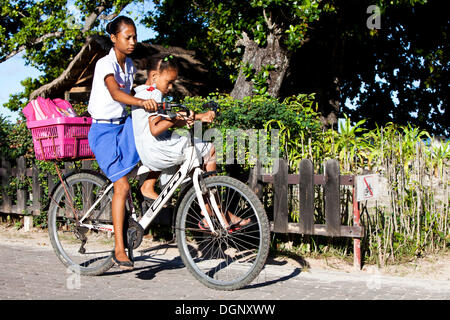 Two girls riding on one bike, La Digue Island, Seychelles, Africa, Indian Ocean Stock Photo