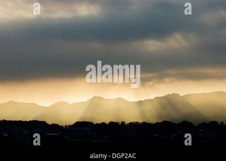 Sunshine coming through gray clouds above mountains Stock Photo