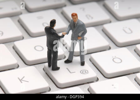Two business men, figurines, shaking hands on the at-key, symbolic image for trading on the Internet Stock Photo