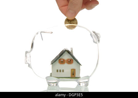 Hand putting coin into piggy bank with a house, symbolic image for building society savings Stock Photo