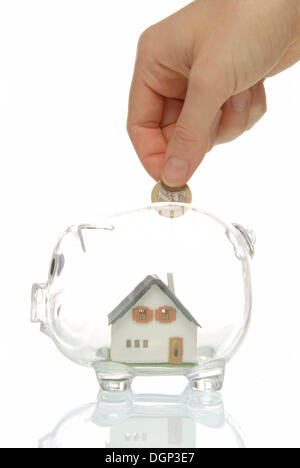 Hand putting coin into piggy bank with a house, symbolic image for building society savings Stock Photo