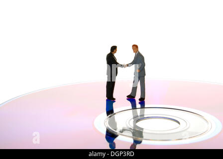 Miniature businessmen figures shaking hands while standing on a data CD Stock Photo