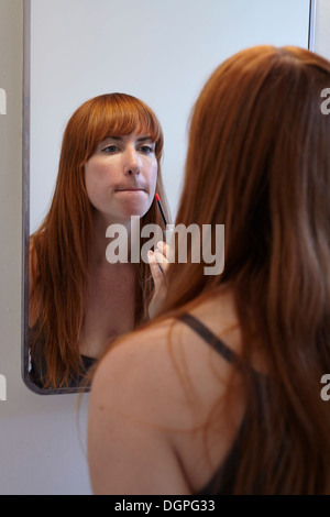 Mid adult woman applying lip gloss in mirror Stock Photo