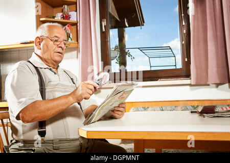 Elderly man reading a newspaper with a magnifying glass Stock Photo