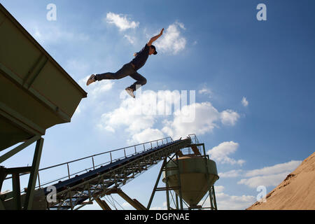 Young man jumping from a conveyor belt into a sand pit, Oettingen, Bavaria Stock Photo