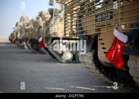A number of British Army tracked armoured vehicles lined up in Afghanistan at Christmas with red stockings hanging from them. Stock Photo