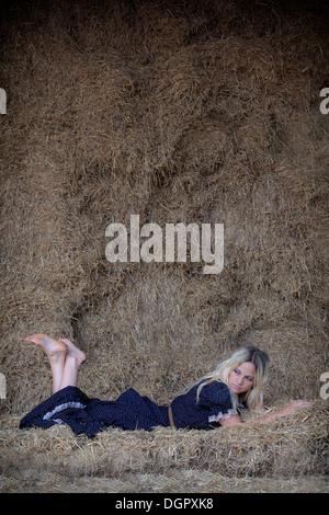 a blond woman is lying in the hay Stock Photo