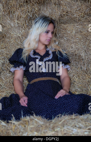 a blond woman is sitting in the hay Stock Photo