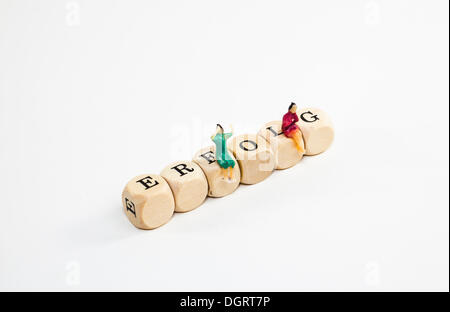 Miniature figures sitting on wooden cubes with letters spelling the word Erfolg, German for success Stock Photo