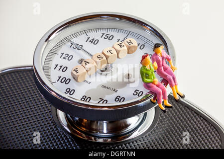 Two women, miniature figures, sitting on the edge of scales, cubes with letters forming the word "Fasten", German for "fasting" Stock Photo