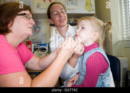 Three and a half year old child, accompanied by her mum / mother, receives a dose of the new flu vaccine - Fluenz - in the form of a nasal spray immunisation from her NHS GP Practice nurse. UK. Stock Photo
