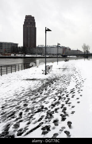 Winter, footprints on the snowy banks of the Main River, historic Weseler Werft wharf, the tower building of the Main Plaza Stock Photo