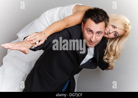 Happy married couple in love bride and groom enjoying flying, woman on male back studio shot gray background Stock Photo