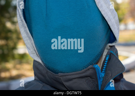 Person with a hidden face concealed under a blue knitted fabric and hood of an anorak, close up view of the head and jacket collar taken outdoors. Stock Photo