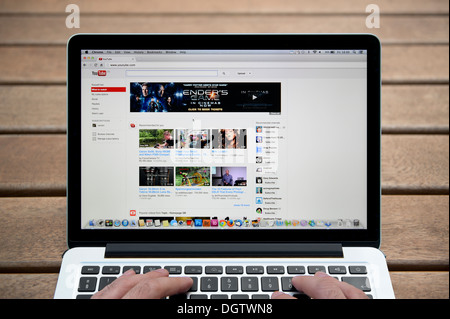 The YouTube website on a MacBook against a wooden bench outdoor background including a man's fingers (Editorial use only). Stock Photo