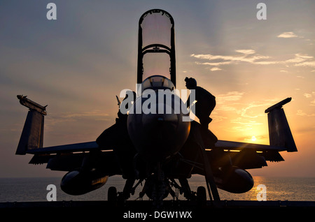 A US Navy Aviation Electronics Technician performs maintenance on an F/A-18F Super Hornet aircraft on the flight deck of the aircraft carrier USS Harry S. Truman at sunset October 11, 2013 in the Gulf of Oman. Stock Photo