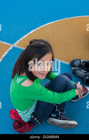 Female teenager sitting on a basketball court looking at camera Stock Photo