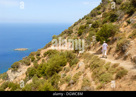 Woman hiking along a steep coastal cliff trail, looking over an island and the blue sea, descending from Moutti tis Sotiras Stock Photo