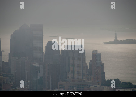 View from the Empire State Building over skyscrapers towards the Statue of Liberty in fog, mist-shrouded Financial District