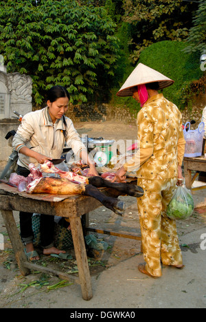 Vietnamese woman wearing a rice hat bargaining with the market saleswoman about the sale of legs of beef Stock Photo