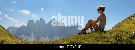 Young woman sitting on a meadow at Mt Aferer Geisler, Odle Massif or Geisler Group at back, Villnöß, South Tyrol province Stock Photo