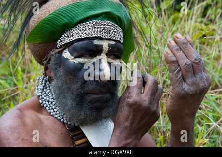 Traditionally dressed tribal chief applying face paint, Hochland, Paya, Highland, Papua New Guinea Stock Photo