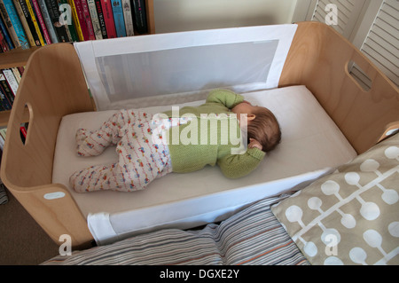 Little baby girl asleep in bedside crib and sucking her thumb Stock Photo