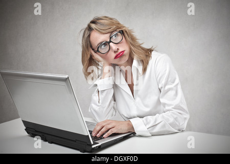 Bored blonde woman with glasses using a laptop Stock Photo