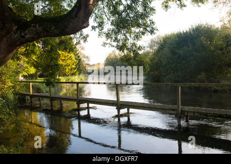 Footbridge over the water as early morning sunshine reflects on the River Test in Hampshire.