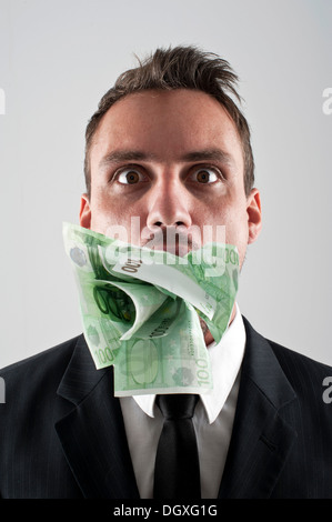Man wearing a suit with 100 € banknotes stuffed in his mouth Stock Photo