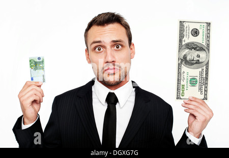 Frustrated young man wearing a suit holding a small 100 euro banknote and a large 100 dollar bill, Austria Stock Photo
