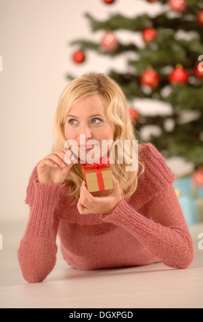 Blonde woman, 20-30, holding a golden gift box, Christmas ambience Stock Photo