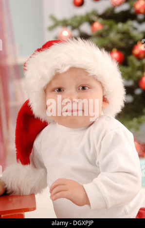Small child with a Santa hat sitting in front of a Christmas tree Stock Photo