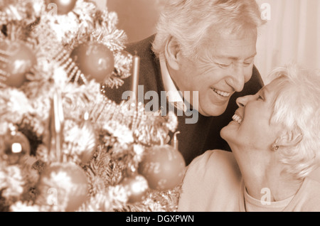 Mature couple looking lovingly at one another beside a Christmas tree Stock Photo