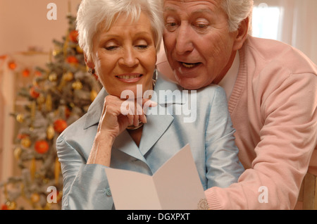 Mature couple reading Christmas cards in front of a Christmas tree Stock Photo