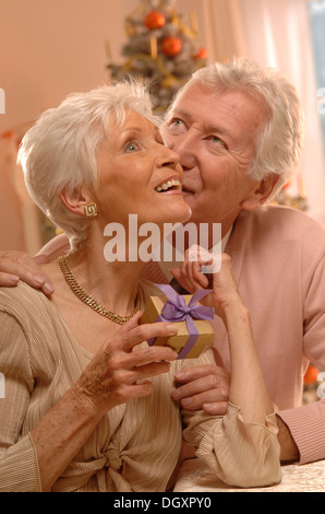 Mature couple exchanging gifts in front of a Christmas tree Stock Photo