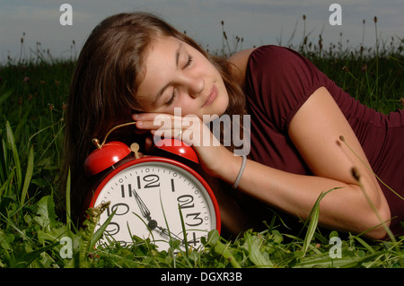Teenage girl lying on the grass and sleeping on an oversized alarm clock Stock Photo
