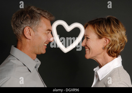 Couple, 35-45, standing face to face and holding a styrofoam heart between their foreheads Stock Photo