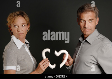Men and women, 35-45, standing next to each other and holding a broken styrofoam heart in their hands Stock Photo