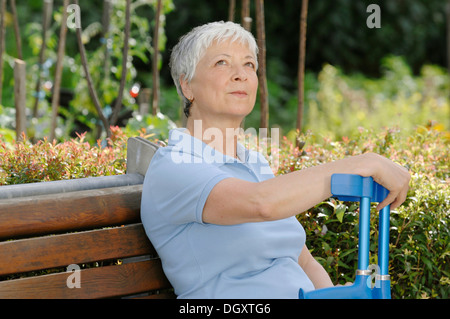 Elderly woman, gray-haired, 55-65, sitting on a park bench with a pair of crutches in her hand Stock Photo
