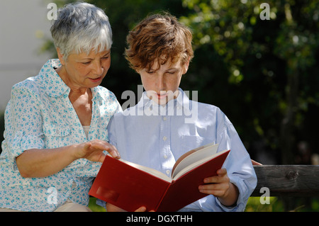 Grandmother and grandson are looking at a red book together on park bench