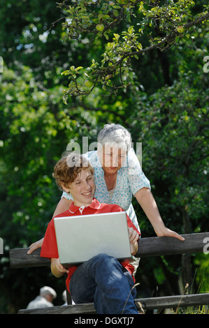 Grandson and grandmother looking together at a laptop computer on a park bench