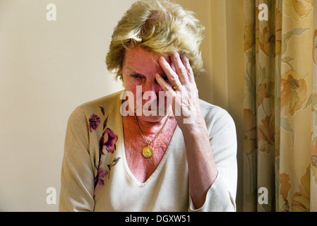 An elderly woman with Dementia and Alzheimer's Disease sitting in her home looking confused and worried. Stock Photo