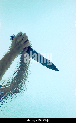 Two raised hands holding a large butcher's knife behind cathedral glass Stock Photo