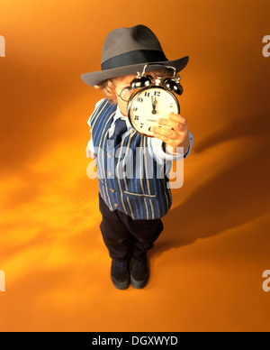 Boy wearing business clothes holding an alarm clock showing eleven fifty-five, just before high noon Stock Photo